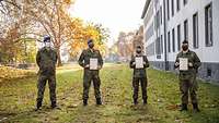 Eine Soldatin und zwei Soldaten halten Urkunden