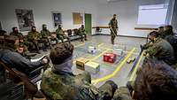 In einem Raum sitzen mehrere Soldaten um eine Modellabbildung des Geländes herum, die auf dem Boden aufgebaut ist.