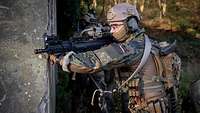 An einer Häuserecke steht ein Soldat mit der Waffe im Anschlag und sichert.