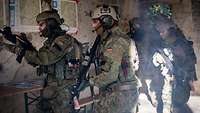 Soldaten stürmen einen Raum in einem alten Gebäude, an der Wand hängen Geländekarten.