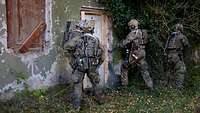 Eine Gruppe von Soldaten steht vor einer Tür, einer schießt mit einer Flinte die Tür auf.