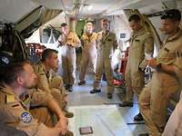 Acht Männer stehen und sitzen im Flugzeug um eine Karte zur Lagebesprechung