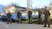 Fünf Soldaten der Bundeswehr stehen mit hinter dem Rücken verschränkten Armen vor parkenden Autos.