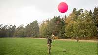 Ein Soldat im Gelände hält einen rosafarbenden Wetterballon