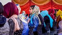 Frauen sitzen vorgebeugt an einer Tafel, in der Mitte hat sich eine Frau zurückgelehnt und spricht in ein Mikrofon