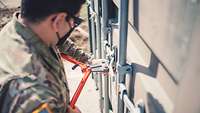 Ein amerikanischer Soldat öffnet mit einem Bolzenschneider einen Container.