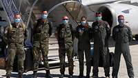 Soldaten stehen mit Mundschutzmaske vor einem Flugzeug.