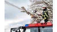 Eine Auszubildende in Feuerwehrmontur bedient ein Wenderohr auf dem Dach eines Feuerlöschfahrzeugs.