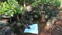 Soldaten betrachten eine Karte, welche auf dem Waldboden liegt.