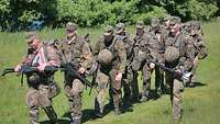 Mehrere Soldaten marschieren in voller Kampfausrüstung durch ein Gelände.