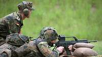 Ein Soldat liegt hinter einem Gewehr. Hinter ihm kniet ein zweiter Soldat.