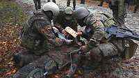 Drei Soldaten knien vor einem verwundeten Soldaten und führen die Triage#fr durch