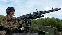 Eine Soldatin steht in der Ladeschützenluke eines Kampfpanzers. Sie bedient ein Maschinengewehr.