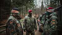 Drei Soldaten mit Tüchern vor Mund und Nase stehen im Wald