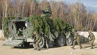 Mehrere Soldaten laufen auf die geöffnete Hecktür eines Militärfahrzeuges zu.