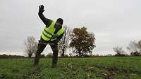 Soldat mit gelber Warnweste und erhobener Hand auf einem Feld.