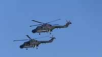 Es sind zwei Hubschrauber in der Luft, leicht versetzt zueinander, zu sehen