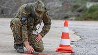Ein Soldat kniet über einem GPS-Empfänger, neben ihm eine Pylone, mit der später der Standort des Startgerätes markiert wird