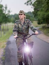 Eine Soldatin fährt auf einem Fahrrad an einem Schild mit der Aufschrift „Bundeswehr“ vorbei.