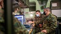 Ein deutscher und ein griechischer Soldat sitzen gemeinsam in einer Kabine an einem Bildschirm