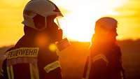 Zwei Soldaten stehen mit Atemschutzmasken vor dem Sonnenaufgang