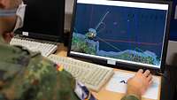 Ein Soldat sitzt vor einem Bildschirm. Dort sind verschiedene Lageinformationen zu sehen