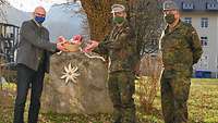 Ein Mann im Trachtenanzug überreicht zwei Soldaten in grüner Uniform einen kleinen Korb.