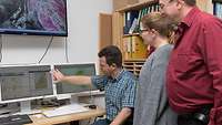 People looking at a monitor with a weather forecast.