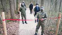 Ein Soldat durchschneidet auf einem Weg ein rotes Band, hinter ihm stehen ein Soldat und drei Zivilisten. 