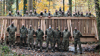 Soldaten mit Mundschutz stehen auf und vor einer neu gebauten Holzbrücke.