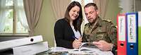Ein Bundeswehrsoldat und eine Frau stehen an einem Tisch mit Ordner und Broschüren