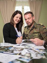 Ein Bundeswehrsoldat und eine Frau stehen an einem Tisch mit Ordner und Broschüren