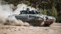 A Puma infantry fighting vehicle drives through the terrain and whirls up dust