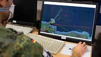Ein Soldat sitzt vor einem Bildschirm. Dort sind verschiedene Lageinformationen zu sehen