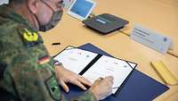Ein Soldat sitzt an einem Schreibtisch und unterzeichnet eine Urkunde