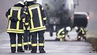Zwei Feuerwehrleute reden miteinander, im Hintergrund schwebt ein Hubschrauber.