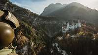 Ein Soldat mit Helm und Sprechsatz blickt aus dem Hubschrauber auf ein weißes Schloss in einer Gebirgslandschaft gelegen.
