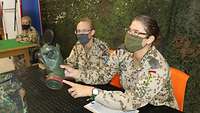 Zwei Soldaten sitzen am Tisch, eine Soldatin hat eine ABC-Schutzmaske in der Hand und überprüft diese 