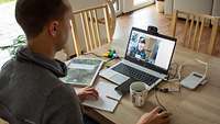 Ein Soldat sitzt in ziviler Kleidung im Homeoffice und hat eine Telefonkonferenz mit seiner Kameradin.