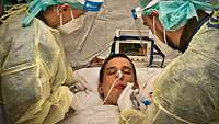 Two soldiers in protective clothing treat an intensive care patient.