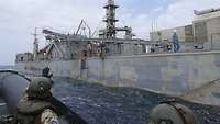 Im Vordergrund ein winkender Soldat im Speedboot, im Hintergrund ein Schiff
