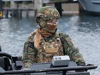 Eine Soldatin mit Helm und Maske steht auf einem Speedboot
