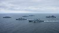 Mehrere graue Kriegsschiffe neben- und hintereinander in See.