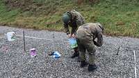 Zwei Soldaten bauen ein Drahtgestell und hängen zwei Eimer daran auf.