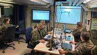 Fünf Soldaten arbeiten an Rechnern im Gefechtsstandzelt, an der Wand leuchten digitale Tafeln.
