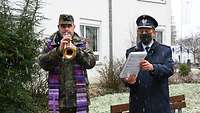 Soldat mit Militärgeistlichem beim Trompetenspiel vor Altersheim.