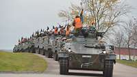 Zahlreiche grüne Schützenpanzer stehen hintereinander auf einer Straße.