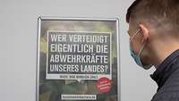 Ein junger Mann mit Maske vor einem Poster