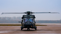 Auf einem leeren Flugfeld steht mittig ein Militärtransporthubschrauber.