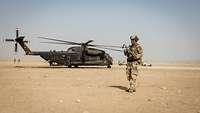 Ein Hubschrauber steht auf dem Wüstenboden, darum herum stehen Soldaten und Fahrzeuge